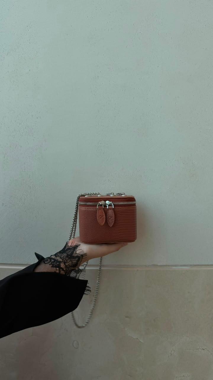 Mini Vanity Chain Bag Brown held by chain strap by hand with black lace sleeve against light blue wall side view