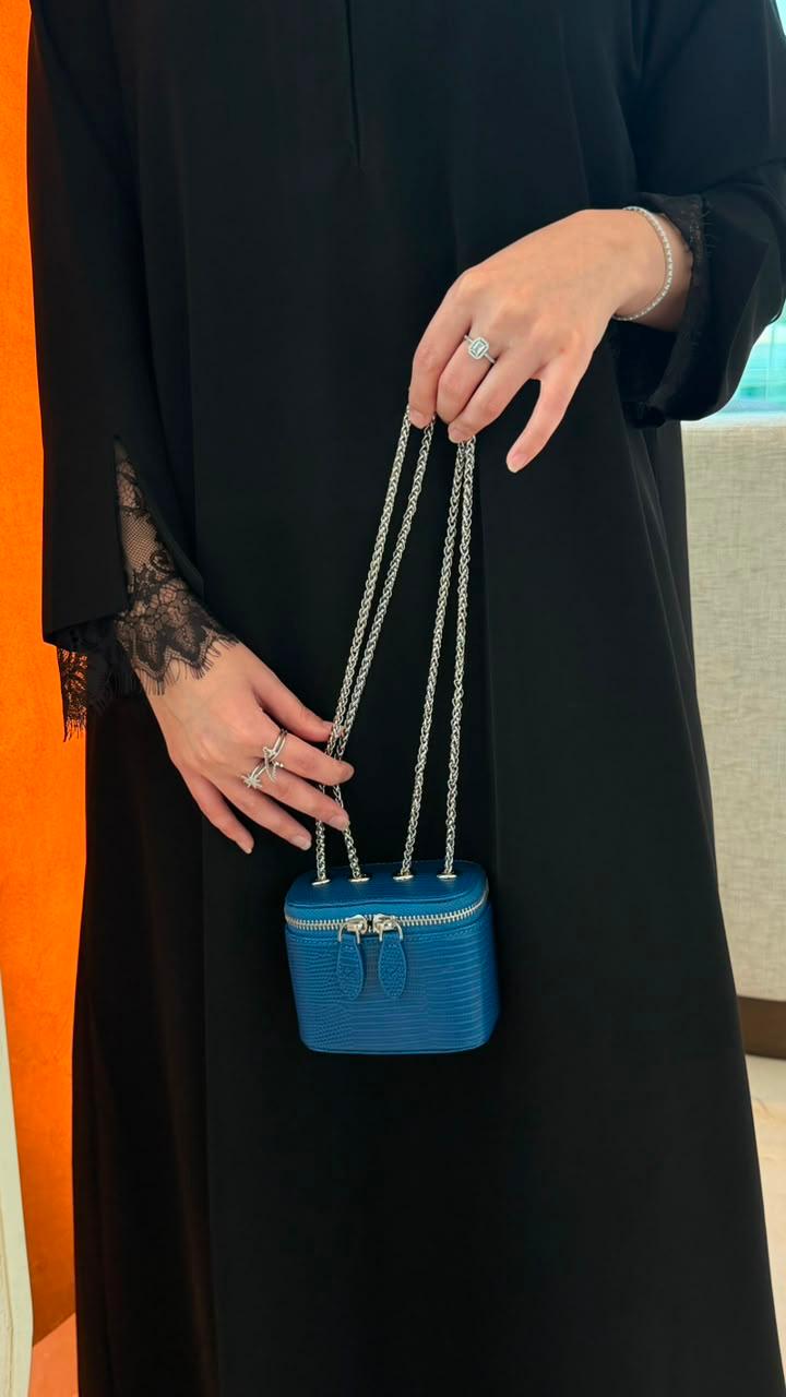 Mini Vanity Chain Bag Royal Blue held by chain strap by woman in black abaya against orange wall side view