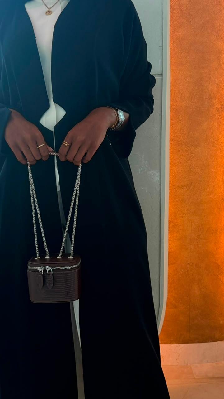 Mini Vanity Chain Bag Espresso held by chain strap by hand with black lace sleeve against light blue wall