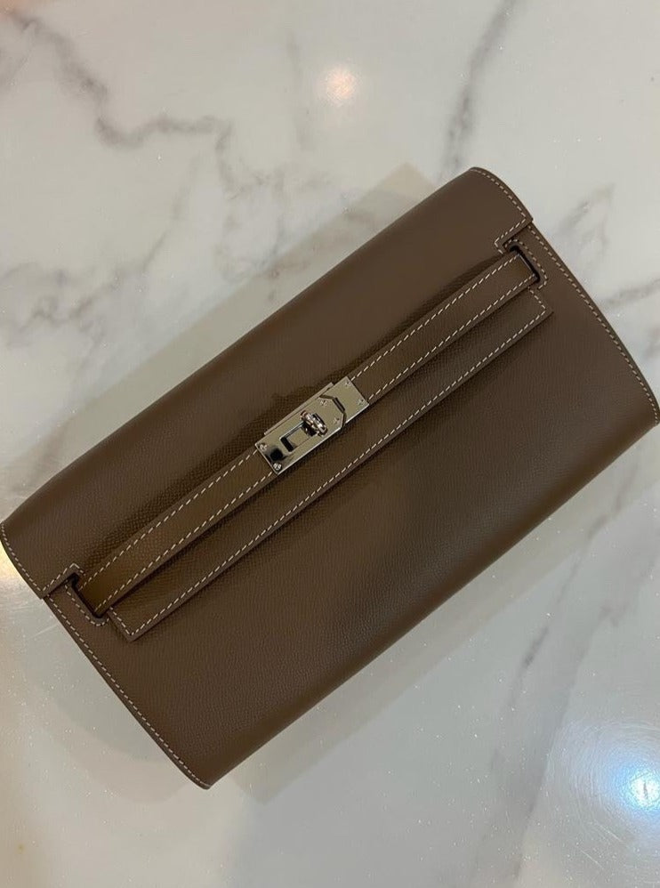 A khaki-colored mini clutch purse placed on a marble surface.