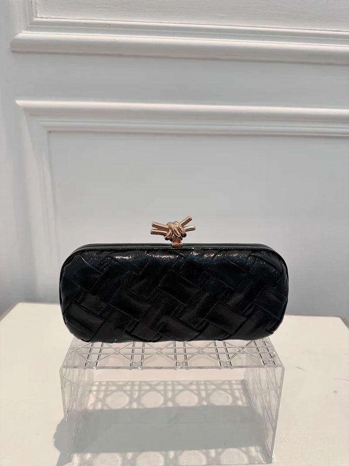 Black quilted clutch bag with a gold clasp on a white surface.