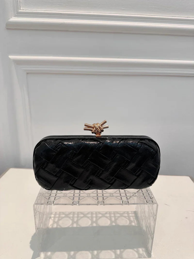 Black quilted clutch bag with a gold clasp on a white surface.