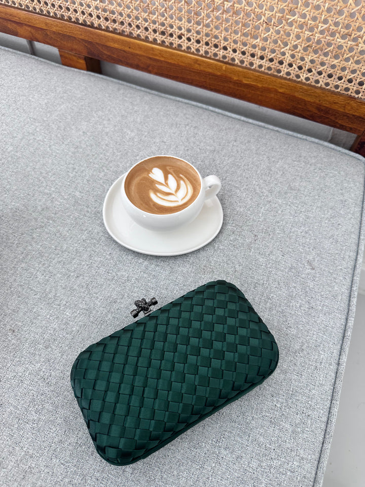 A green quilted leather clutch bag placed on a table beside a cup of coffee.