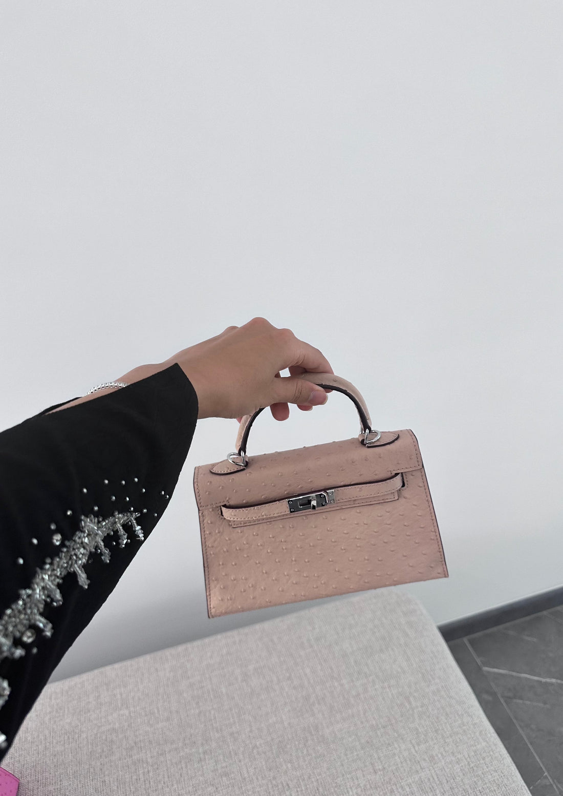 A person holding a beige handbag with a clear logo and a long strap, suitable for carrying various personal items.