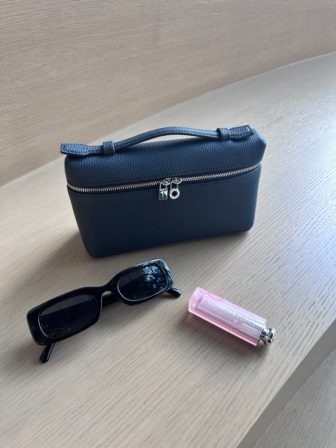 A navy-colored bag with a zipper and a metallic clasp, accompanied by sunglasses and a pink cylindrical object, presumably the product referred to as 'lp-neavy blue'.