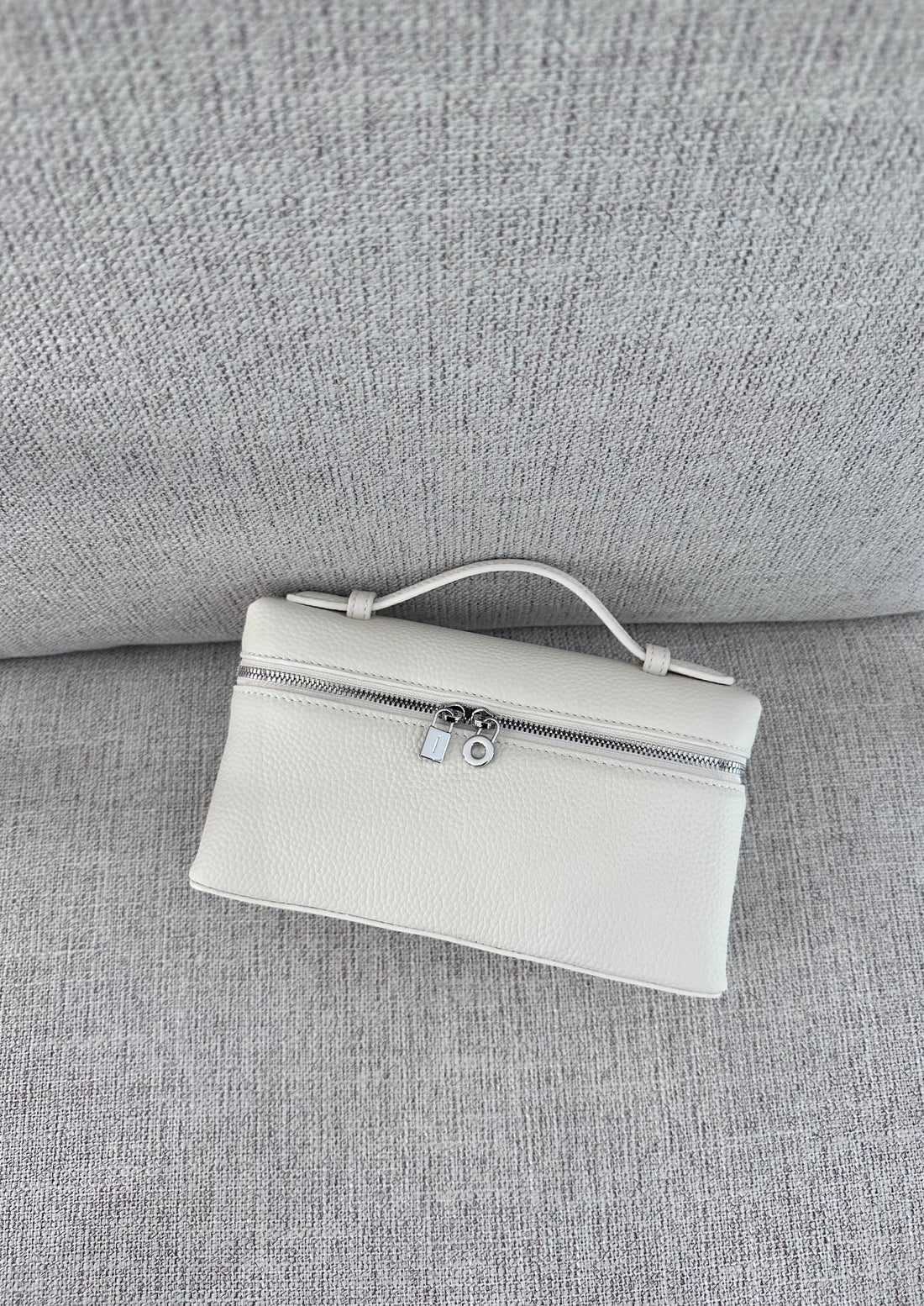 A white tote handbag with a minimalist design, placed on a grey textured surface.