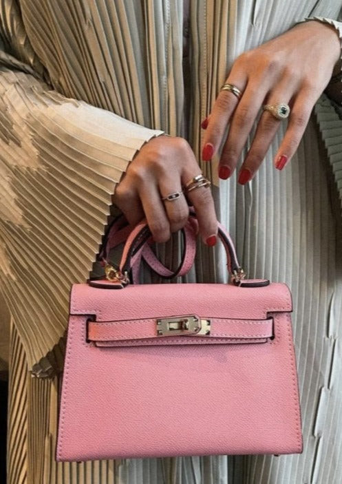 A person holding a small blush pink handbag with a strap.