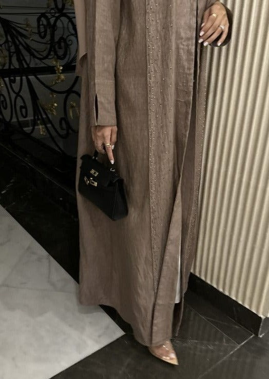 A person wearing a long brown dress holding a black clutch purse with a long strap.
