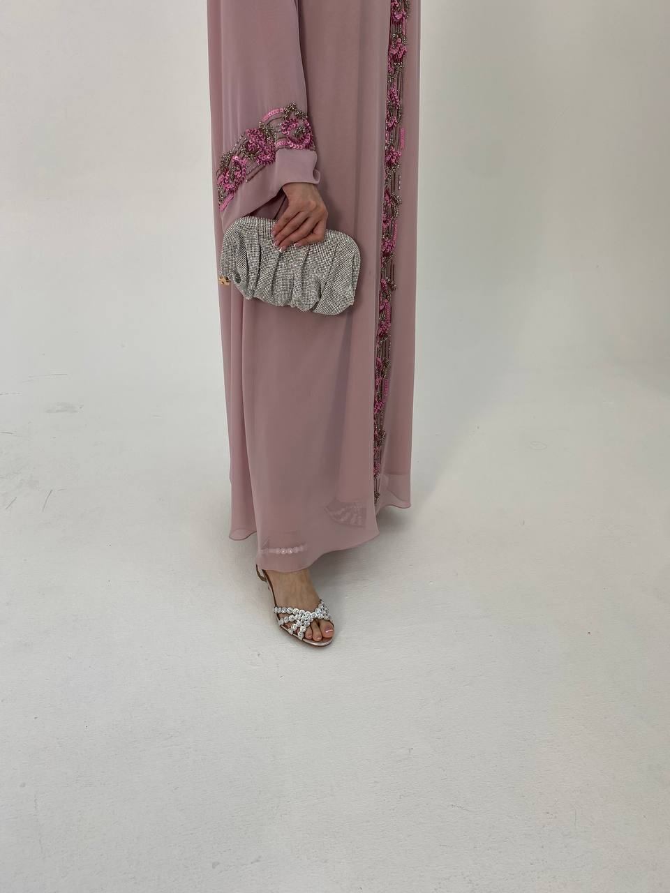 Person wearing a long, light pink dress with floral embroidery on a plain background