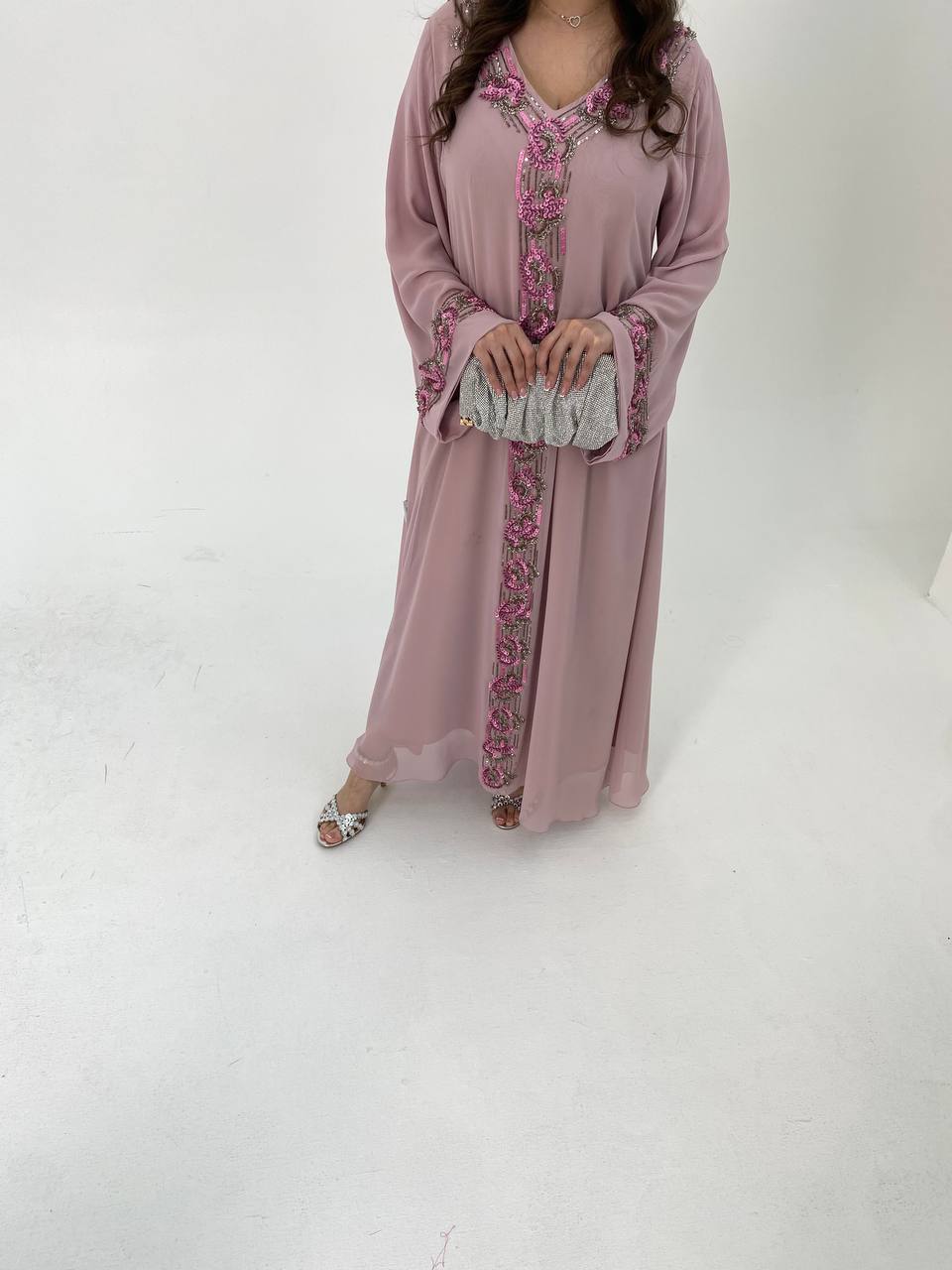 Woman wearing a long, light pink dress with floral embroidery on a white background