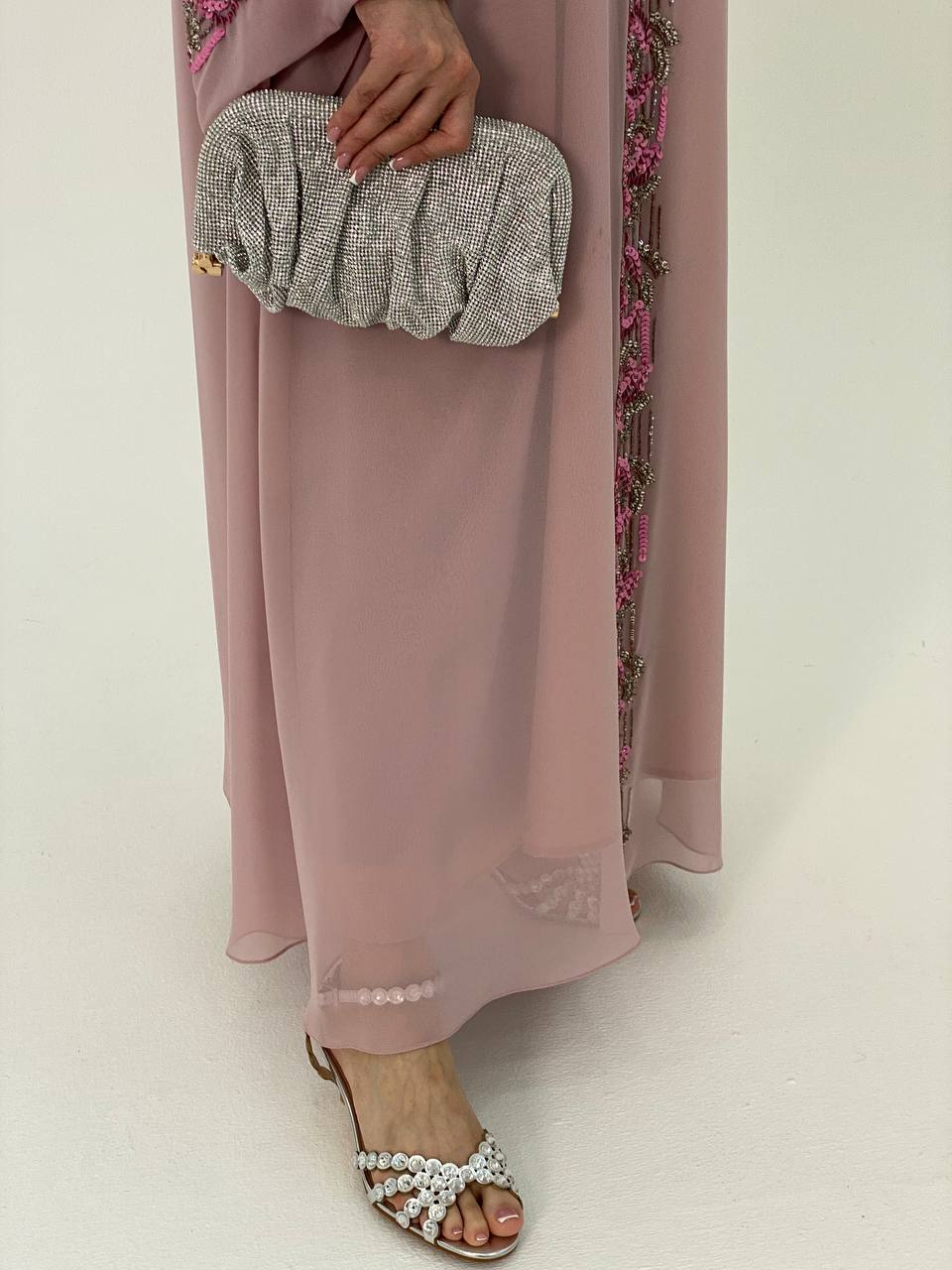Person wearing a pink outfit with a textured clutch and sandals on a white background